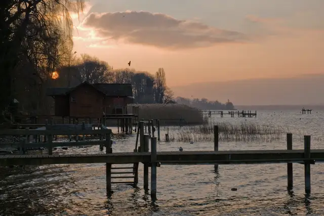 A lakeside house and wooden footbridge at sunset