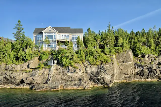 A house on a rocky shoreline above dark water with stairs down to the water