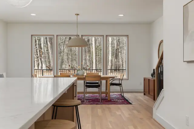 A dining room with tall windows facing evergreen trees