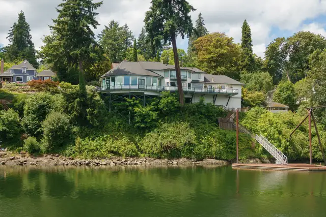 A modern house with long windows set among evergreens above a green lake shore