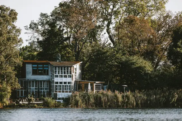 A white modern house on the water framed by old trees