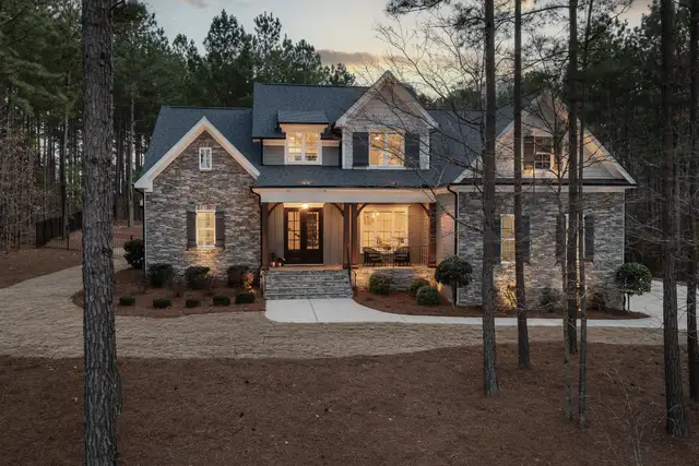 A stone house with lit windows among tall pines at dusk