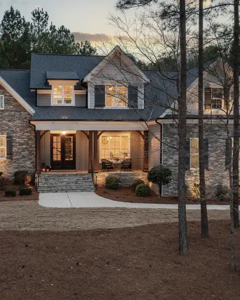 A stone house with lit windows among tall pines at dusk